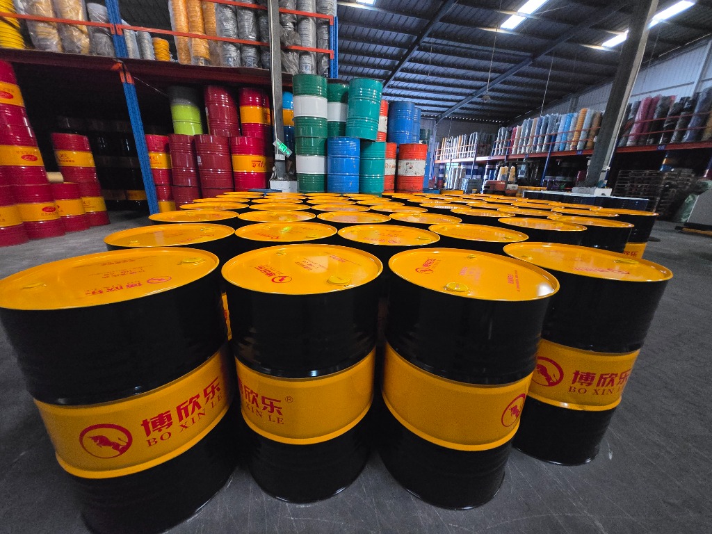 Staged rows of black and yellow industrial hydraulic oil drums with multi-tier colored storage racking in background